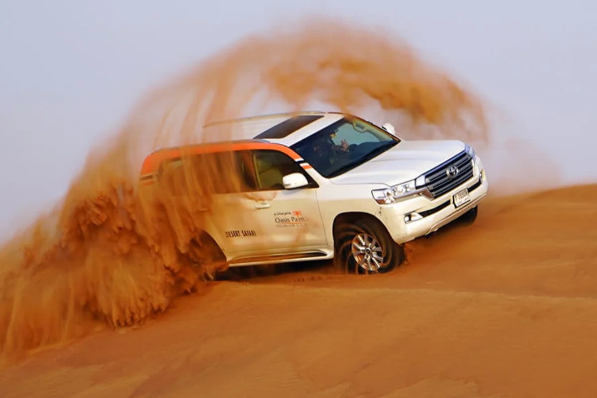 A 4x4 vehicle driving over desert dunes at sunset.